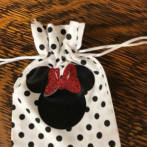 Puede incluir: Una bolsa de cord&oacute;n blanca con lunares negros y una silueta de Minnie Mouse negra y roja.