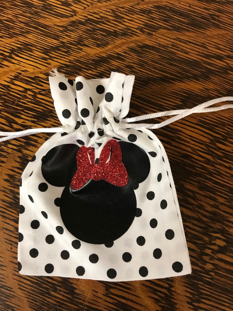 Puede incluir: Una bolsa de cord&oacute;n blanca con lunares negros y una silueta de Minnie Mouse negra y roja.