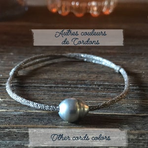 Puede incluir: Una pulsera plateada con una gran perla gris en el centro. El cordón de la pulsera es de material metálico tejido. La imagen incluye el texto "Autres couleurs de Cordons" y "Other cords colors".