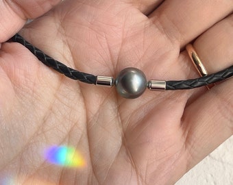 Collana realizzata con una bellissima perla di Tahiti semirotonda su pelle nera intrecciata rotonda. Chiusura in acciaio