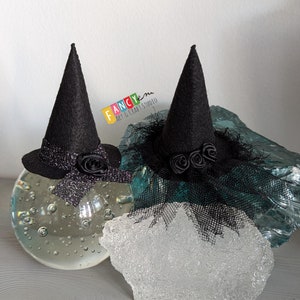 May include: Two black felt witch hats with black tulle and black rose embellishments. The hats are sitting on a clear glass surface.