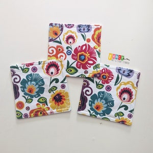May include: Three square fabric coasters with a white background and colorful floral patterns. The coasters have a yellow border and are sewn with a dark grey thread.