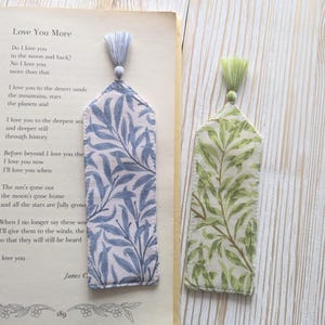 May include: Two fabric bookmarks with pointed tops and matching tassels. One bookmark features a blue and white willow leaf pattern, while the other displays a green and cream willow leaf pattern. The blue bookmark rests on an open book page.