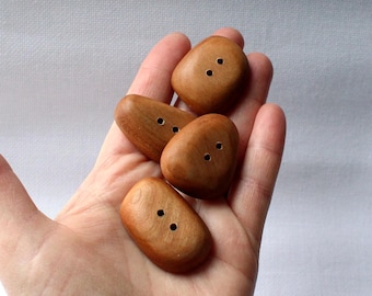 May include: Four wooden buttons in a hand. The buttons are brown and have two holes each. They are shaped like rounded rectangles.