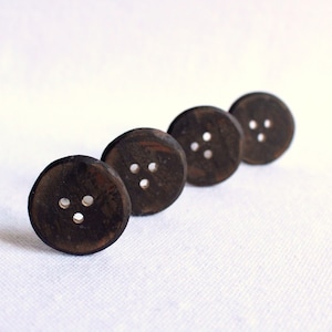 May include: Four dark brown wooden buttons with three holes each are arranged diagonally on a white surface. The buttons have a natural wood grain pattern and a slightly rounded shape, suggesting they are handmade.