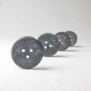 May include: Four dark grey buttons with a speckled finish and three holes each. The buttons are arranged in a row, with the largest button on the left and the smallest button on the right.