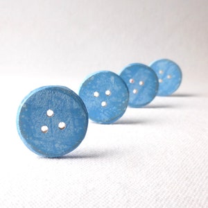 May include: Four light blue wooden buttons with two holes each, arranged in a row on a white surface.