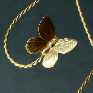 Puede incluir: Un colgante de mariposa de color dorado cuelga de una cadena dorada trenzada. La mariposa tiene alas detalladas y un cuerpo texturizado.
