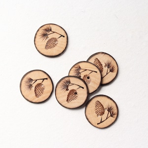 May include: Six wooden buttons with a pine cone and branch design. The buttons are round and have a natural wood color.