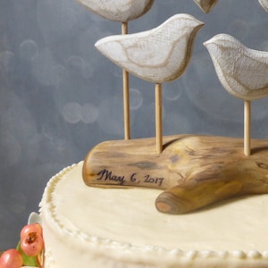 May include: A white wedding cake with a wooden log base and three white wooden birds perched on top. The log base is inscribed with the date "May 6, 2017".