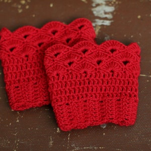 May include: Two red crocheted boot cuffs with a scalloped edge and a lacy pattern.