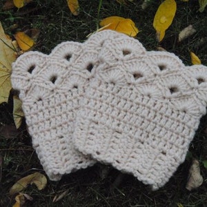 May include: A pair of crocheted leg warmers with a scalloped edge and a delicate openwork pattern. The leg warmers are a light cream colour.