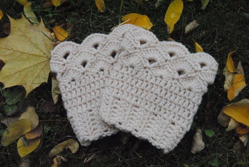 May include: A pair of crocheted leg warmers with a scalloped edge and a delicate openwork pattern. The leg warmers are a light cream colour.