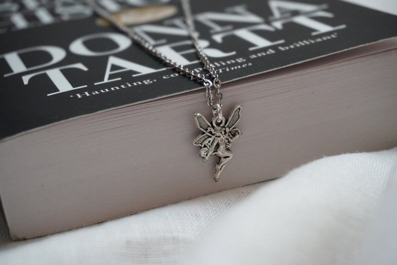 Peut inclure: Un collier en argent avec un pendentif en forme de f&eacute;e. Le collier est pos&eacute; sur un livre intitul&eacute; "Donna Tartt" avec la citation "Haunting, compelling and brilliant" du Times.