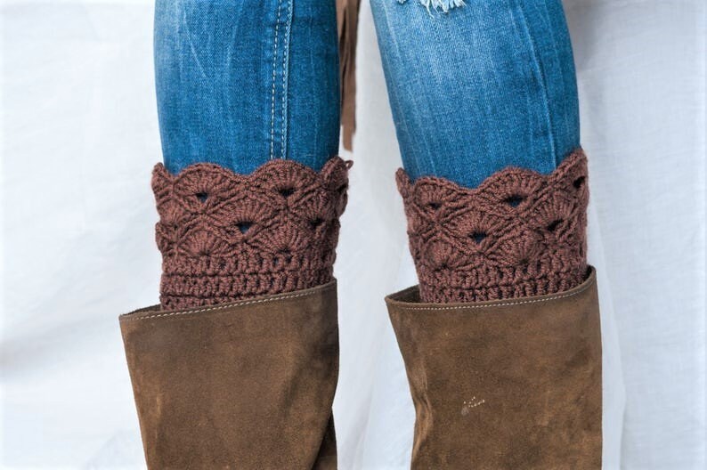 May include: Brown crocheted boot cuffs with a scalloped edge. The cuffs are worn over brown suede boots and blue jeans.