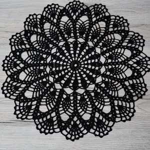 Könnte beinhalten: Eine schwarze Häkeldeckchen mit einem runden Design. Die Deckchen hat ein zartes, filigranes Muster mit einem zentralen Motiv.