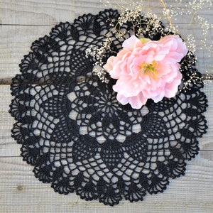 Puede incluir: Un encaje de ganchillo negro con un delicado patrón floral, con una flor rosa y aliento de bebé blanco sobre un fondo de madera.