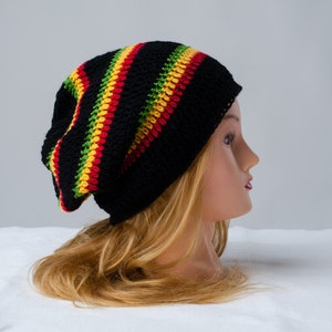 Op de afbeelding: Een zwarte gehaakte beanie met rode, gele en groene strepen. De beanie wordt gedragen door een mannequin met lang blond haar.