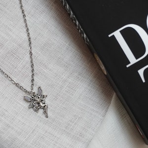 Peut inclure: Un collier en cha&icirc;ne argent avec un pendentif en forme de f&eacute;e. La f&eacute;e est repr&eacute;sent&eacute;e avec des ailes et une robe flottante.