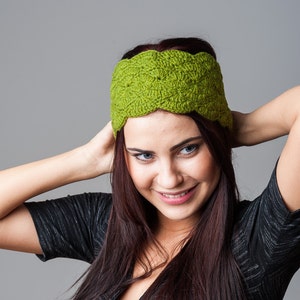 Peut inclure: Une femme aux longs cheveux bruns fonc&eacute;s porte un bandeau crochet&eacute; vert. Elle porte un chemisier noir et a une expression neutre sur son visage.