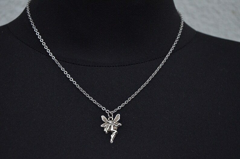 Peut inclure: Un collier en cha&icirc;ne argent&eacute;e avec un pendentif en forme de f&eacute;e. La f&eacute;e est repr&eacute;sent&eacute;e avec des ailes et une robe flottante.