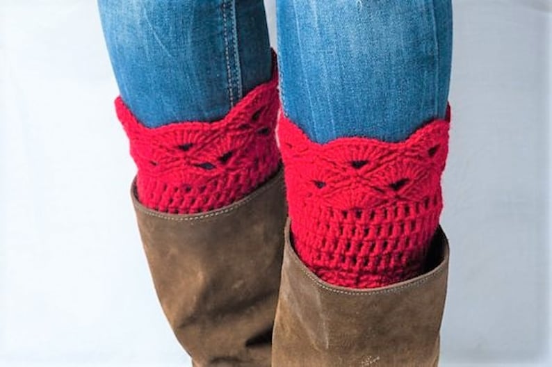 May include: Red crocheted boot cuffs with a lacy design. The cuffs are worn over brown boots and blue jeans.