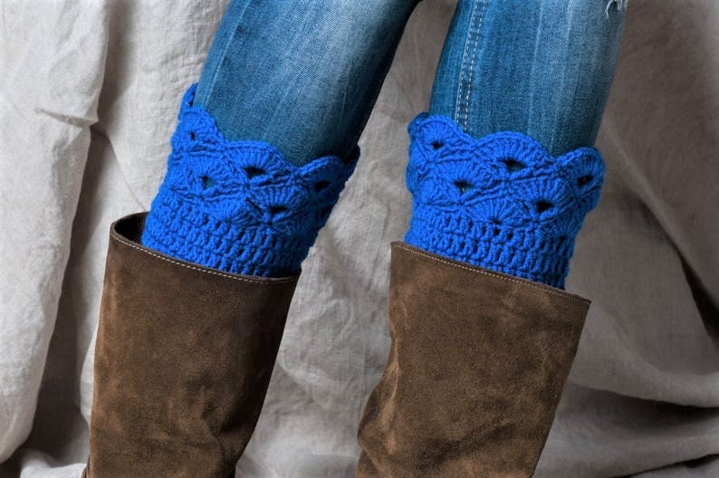May include: A pair of blue crocheted leg warmers with a scalloped edge. The leg warmers are worn over brown suede boots and blue jeans.