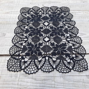 Puede incluir: Camino de mesa de crochet negro con un delicado patrón floral. El camino de mesa está hecho de hilo fino y tiene un borde festoneado.