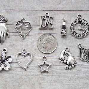 May include: A collection of 12 silver charm pendants featuring various designs, including a hand, diamond, heart, star, clock, flower, footprint, and a book with the word "LOVE" on it.