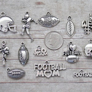 May include: A collection of silver-toned football-themed charms. The charms include a football helmet, a football player, footballs, and text that says "I Love Football", "Go Team", "Football Mom", and "Football".