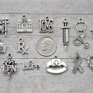 May include: A collection of silver-toned charms with medical themes, including a hospital building, a stethoscope, a syringe, a cross, a pill bottle, a caduceus, a nurse's cap, an LPN symbol, a ribbon, a heart, and the words "love" and "hope".