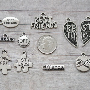 May include: A collection of silver-toned friendship charms with various designs and text. Charms include the words "BEST FRIENDS", "FRIENDS", and "BFF". Other charms feature puzzle pieces and a broken heart design. A US dime is included for size reference.