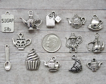 May include: A collection of 14 silver charm pendants featuring teapots, teacups, a cupcake, a spoon, and a sugar packet that says "Sugar 5lb".