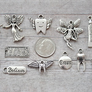 May include: A collection of silver-toned charms with dental and inspirational themes. Charms include a tooth with wings, a toothbrush, a tube of toothpaste, a smiley face, a star wand, and the word "believe".