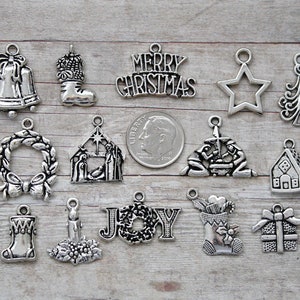 May include: A collection of silver-toned Christmas charms, including Santa, a bell, a stocking, and a "Merry Christmas" banner. Other charms include a star, tree, candy cane, wreath, and a nativity scene. A dime is included for size reference.