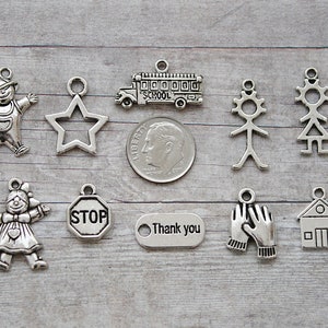May include: A set of ten silver charm pendants featuring various designs, including a school bus, a star, stick figures, a stop sign, a house, and a thank you tag.