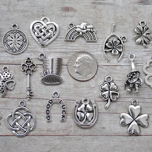 May include: A collection of 17 silver charm pendants featuring Irish symbols like shamrocks, horseshoes, and Celtic knots. The charms are arranged on a wooden surface.