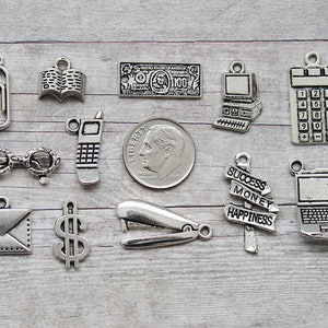 May include: A collection of 12 silver charm pendants featuring various office-themed designs, including a paperclip, book, dollar bill, computer, calculator, phone, glasses, envelope, dollar sign, stapler, signpost with the words "Success, Money, Happiness", and a laptop.