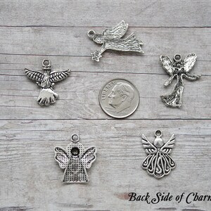 K&ouml;nnte beinhalten: F&uuml;nf silberne Engelscharms, jeder mit einem anderen Design, werden auf einer Holzoberfl&auml;che gezeigt. Eine Zehn-Cent-M&uuml;nze ist zum Gr&ouml;&szlig;envergleich enthalten. Die R&uuml;ckseite der Charms ist im Bild zu sehen. "Back Side of Charms" steht am unteren Rand des Bildes.