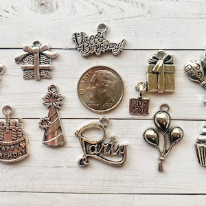 May include: A collection of silver-toned metal charms with birthday themes. The charms include a cake, balloons, a party hat, a gift box, and the words "Happy Birthday" and "Party".