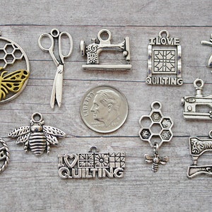 May include: A collection of silver and gold-toned metal charms featuring bees, honeycombs, sewing machines, scissors, and the phrase "I Love Quilting".