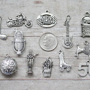 May include: A collection of silver-toned charms featuring a musical note, motorcycle, musical notes, guitar, jukebox, microphone, hot dog, hamburger, milkshake, fries, roller skate, poodle, and the number 50.
