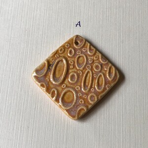 May include: A brown ceramic tile with a raised pattern of circles and ovals. The tile is in the shape of a diamond.