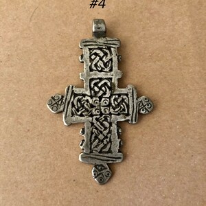 May include: A silver pendant in the shape of a cross with intricate knotwork designs. The cross is about 2 inches tall and has a loop at the top for hanging.