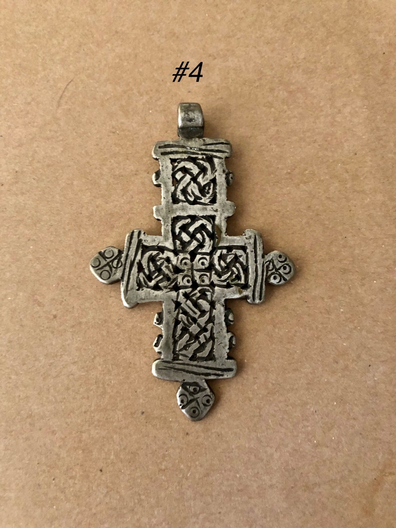 May include: A silver pendant in the shape of a cross with intricate knotwork designs. The cross is about 2 inches tall and has a loop at the top for hanging.