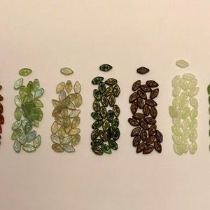 Könnte beinhalten: Sortiment aus acht Reihen kleiner Glasblätter in verschiedenen Grüntönen, Braun- und Weißtönen.