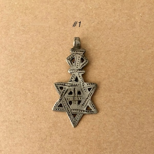 May include: A silver pendant featuring a six-pointed star with intricate details. The star is topped with a small, ornate crown.