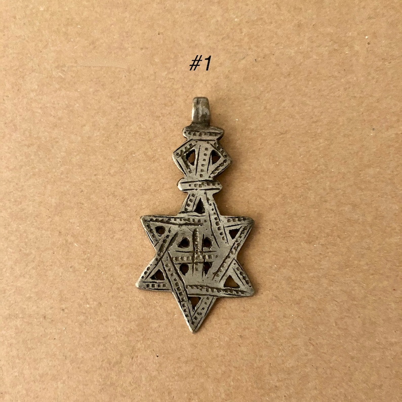 May include: A silver pendant featuring a six-pointed star with intricate details. The star is topped with a small, ornate crown.