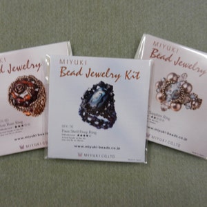 May include: Three white card packages with images of beaded jewelry kits. The packages are labeled "MIYUKI Bead Jewelry Kit" and include the names of the kits: "Rose Rose Ring", "Paus Shell Deep Ring", and "Sapphire Ring".