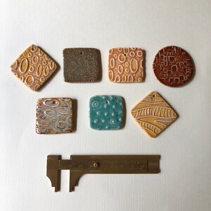 May include: Seven ceramic tiles with different patterns and colors. The tiles are square, diamond, and round shapes. The colors include brown, blue, yellow, and white.